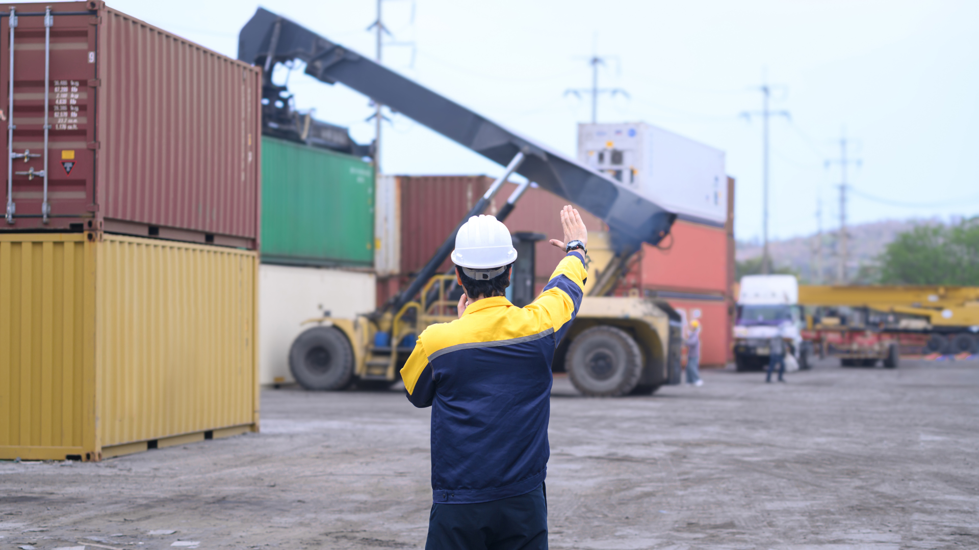 Profissional de logística orienta a movimentação de contêineres em um terminal de cargas, destacando a importância da coordenação operacional para identificar e reduzir gargalos na sua operação, aumentando a eficiência da cadeia logística.