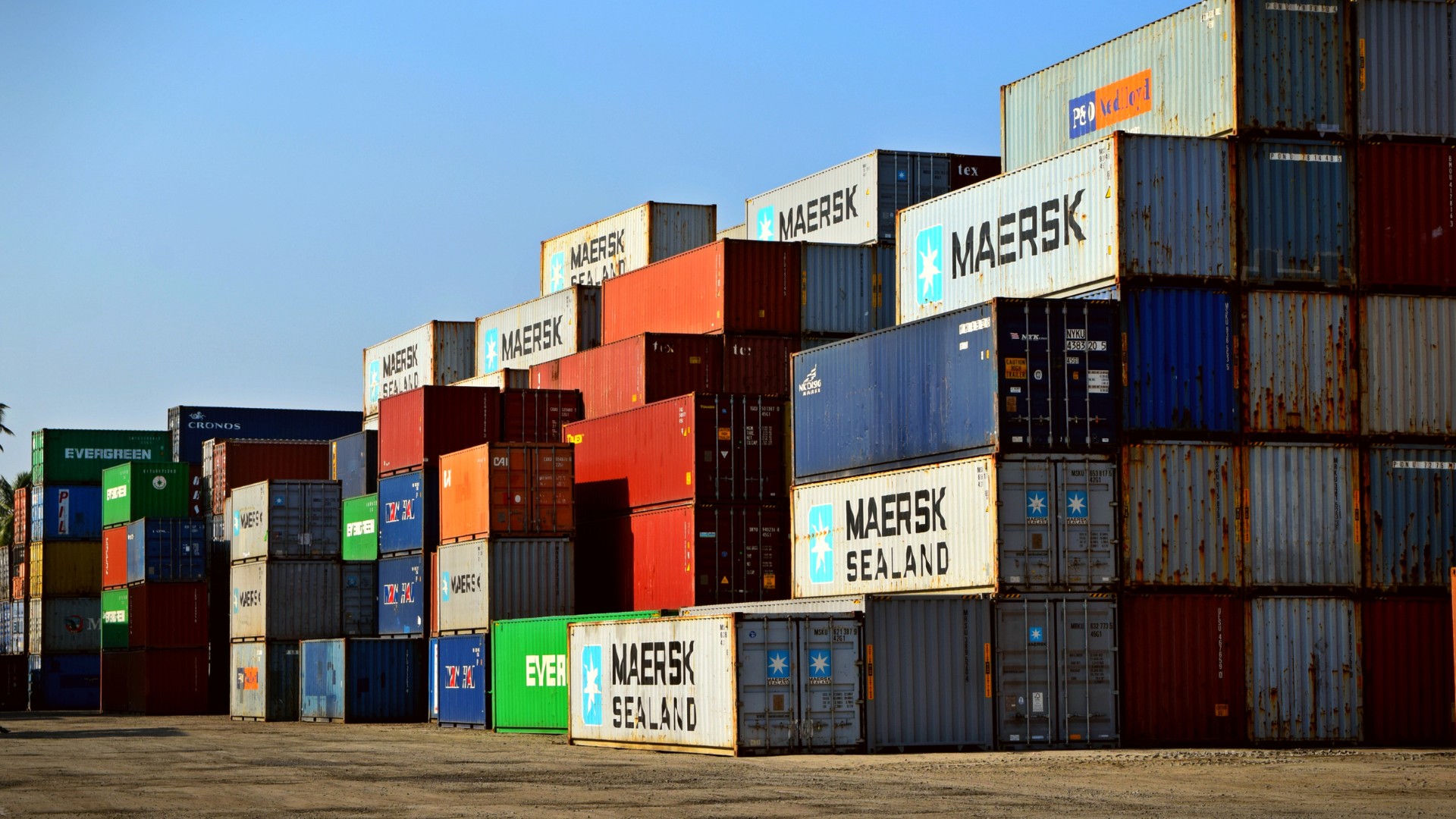 Contêineres de carga empilhados em um terminal logístico, representando operações de comércio exterior e regimes aduaneiros como Drawback e RECOF.
